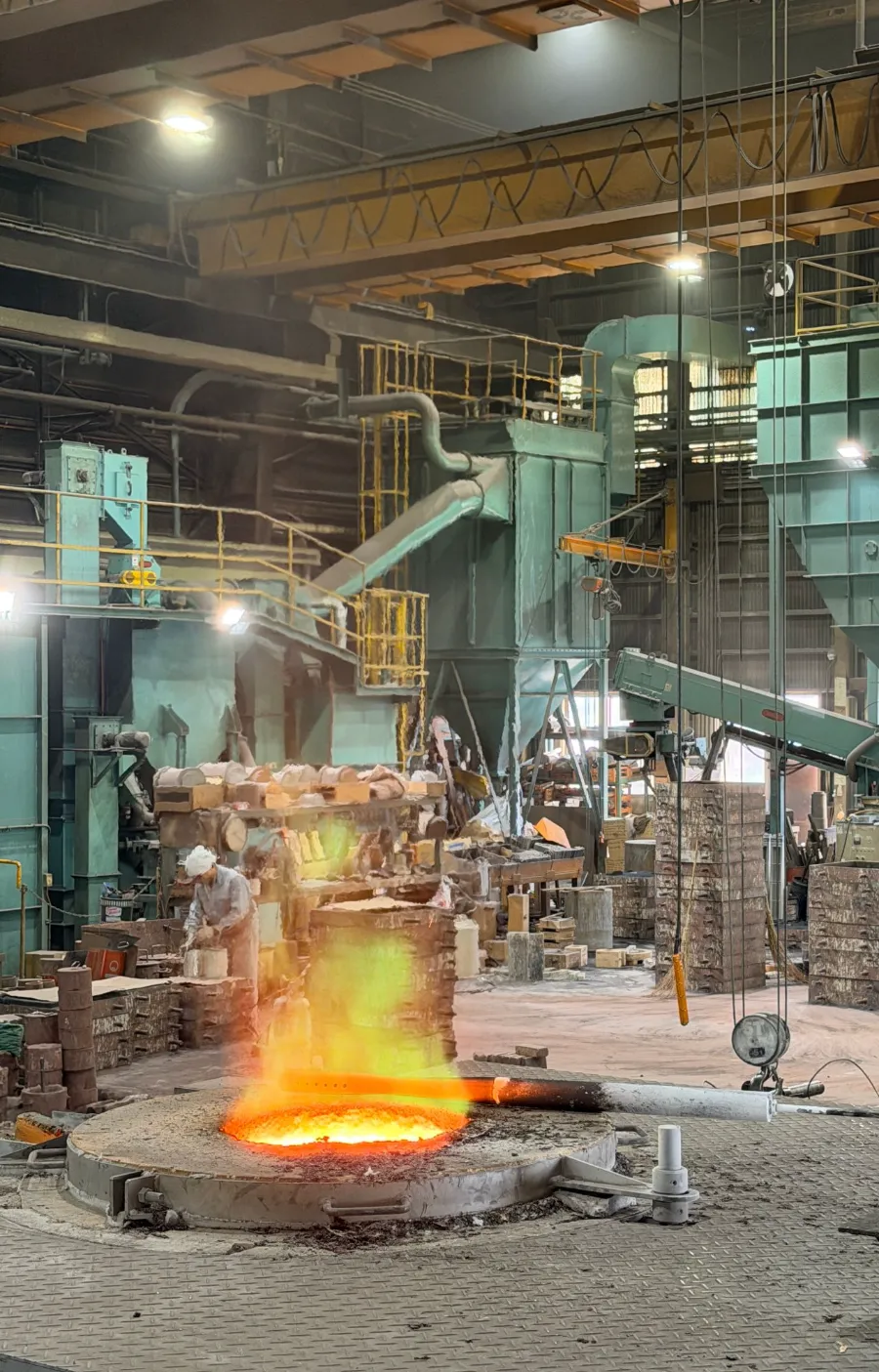 Inside the Ueda Metal Works Co., Ltd. factory: metal glows red in a furnace in front, while workers make molds in the back